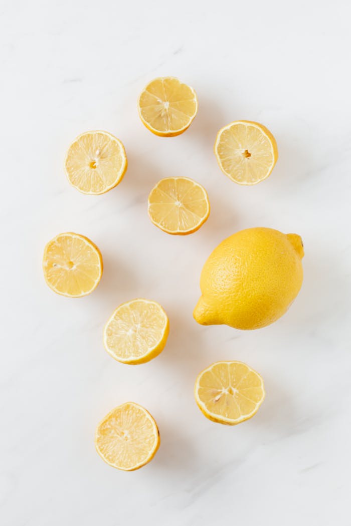 A flat lay of whole and sliced fresh lemons on a clean marble surface.